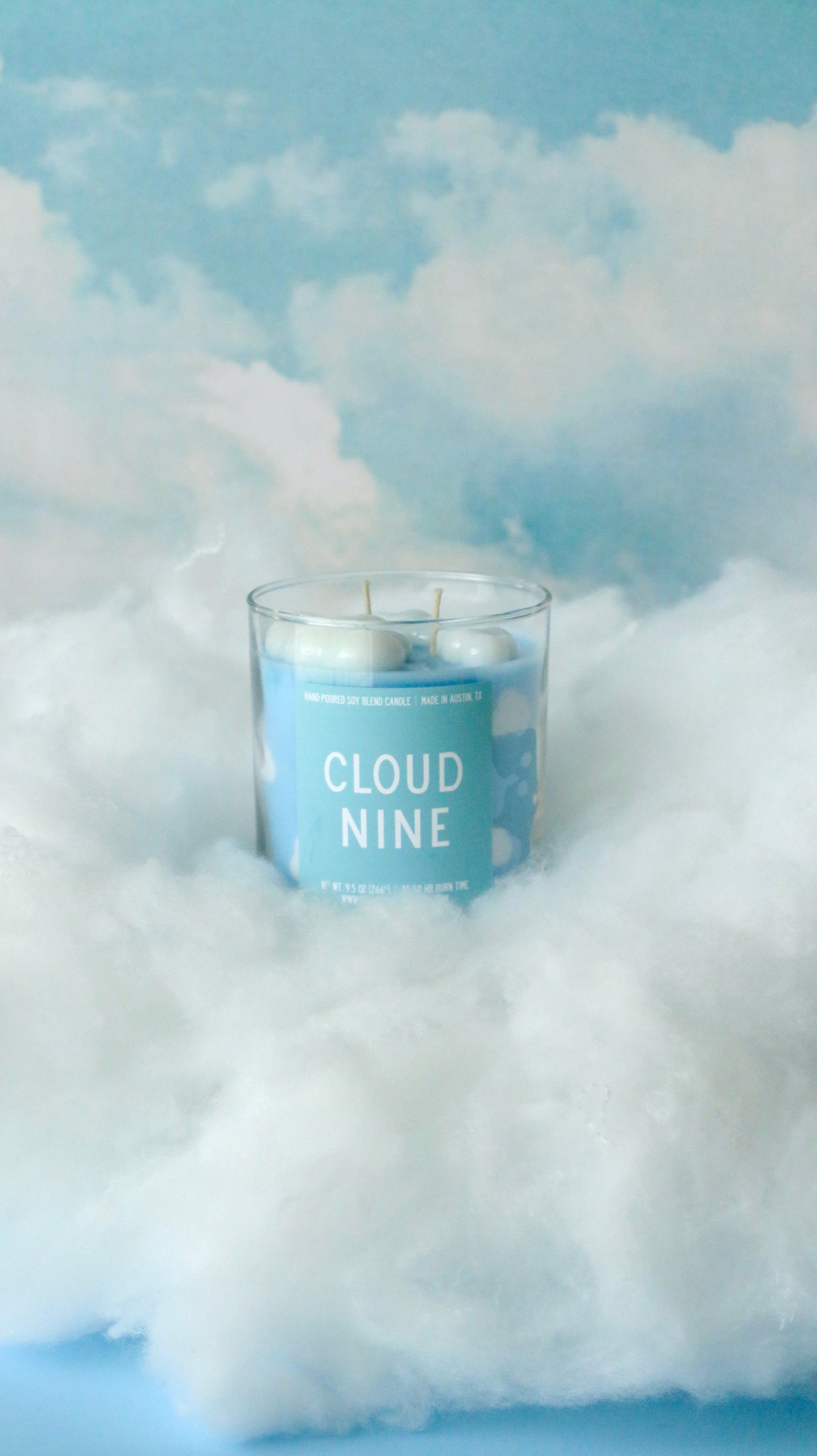 Candle labeled 'Cloud Nine' surrounded by fluffy white clouds against a blue sky.
