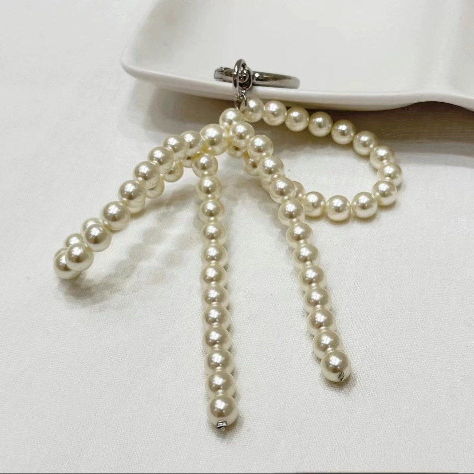Close-up of a hand-woven pearl white bow charm attached to a cream-colored leather handbag, showcasing the coquette aesthetic