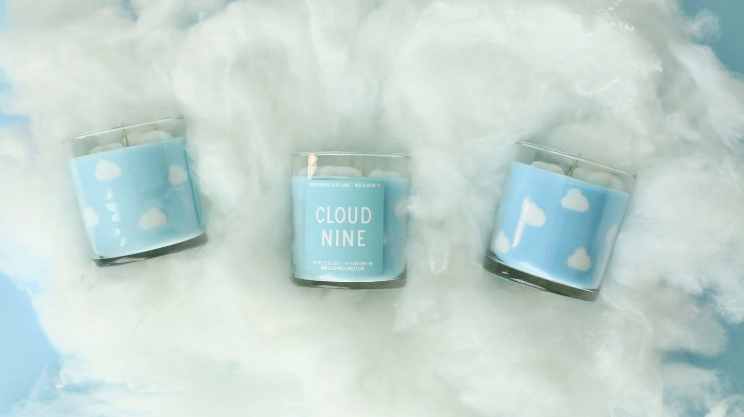 Three candles labeled 'Cloud Nine' with blue labels featuring white clouds on a fluffy white background.