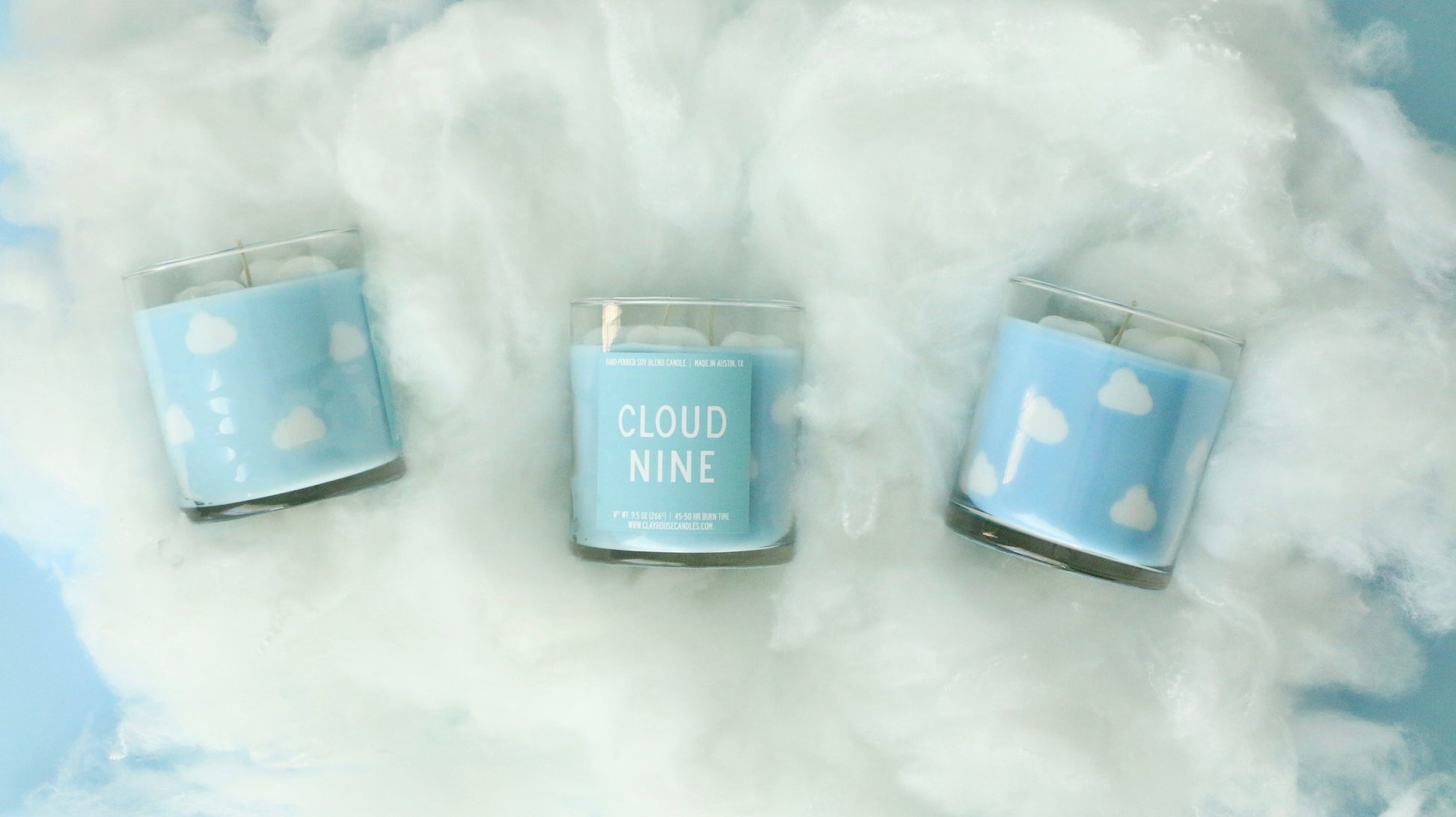Three candles labeled 'Cloud Nine' with blue labels featuring white clouds on a fluffy white background.