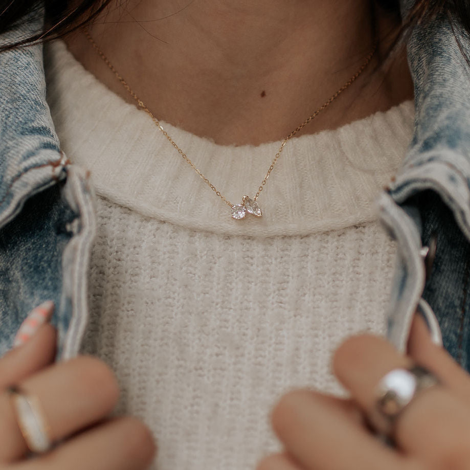 Person wearing a delicate necklace with a small pendant, holding scissors.