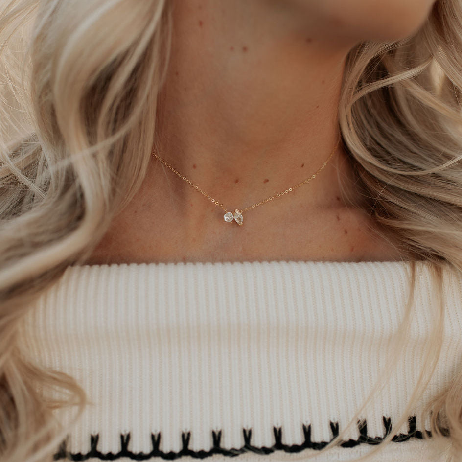 Close-up of a woman wearing a delicate gold necklace with a small pendant, against a neutral background.