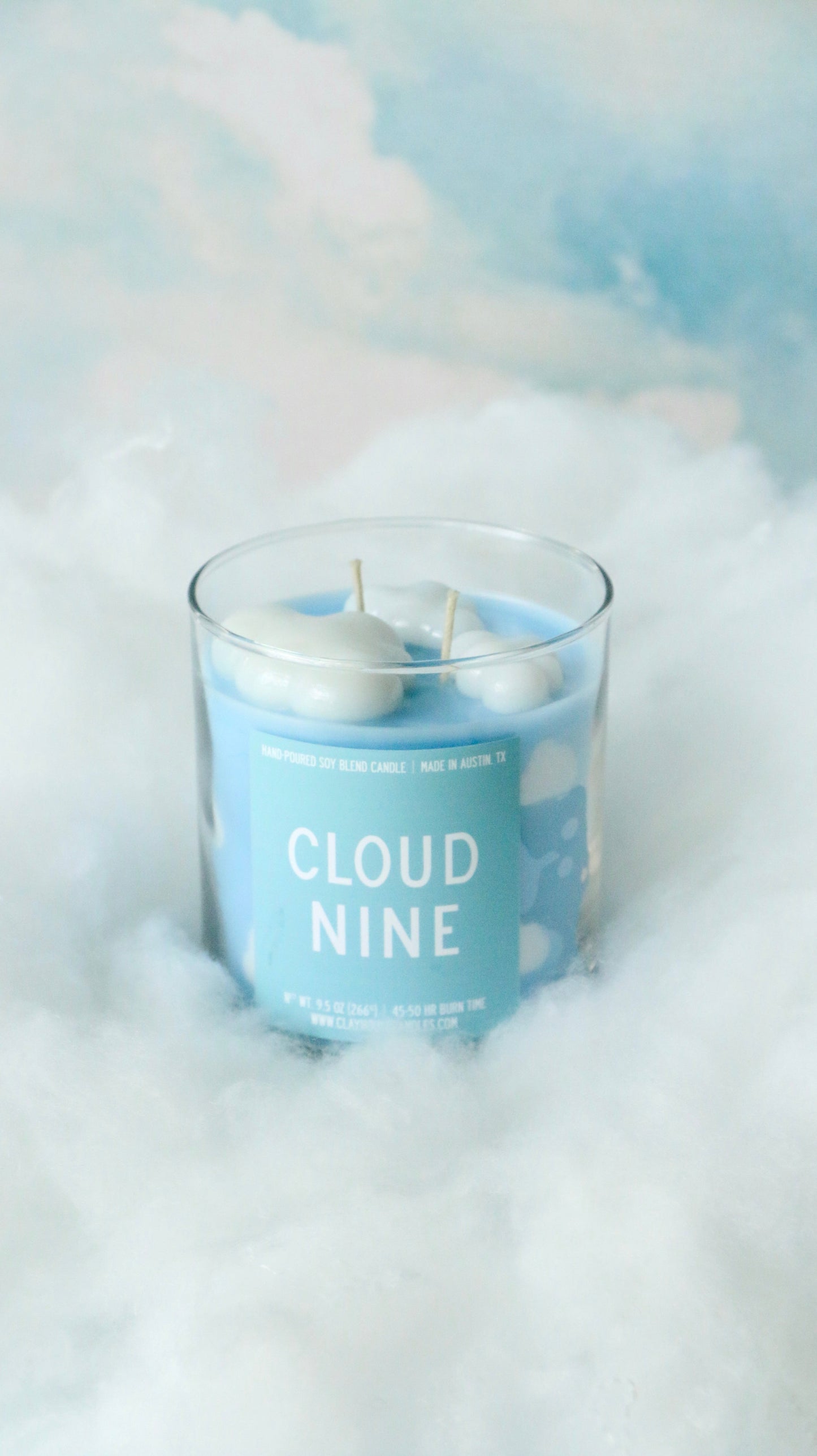 Candle labeled 'Cloud Nine' with a cloud-themed label on a soft, cloud-like background.