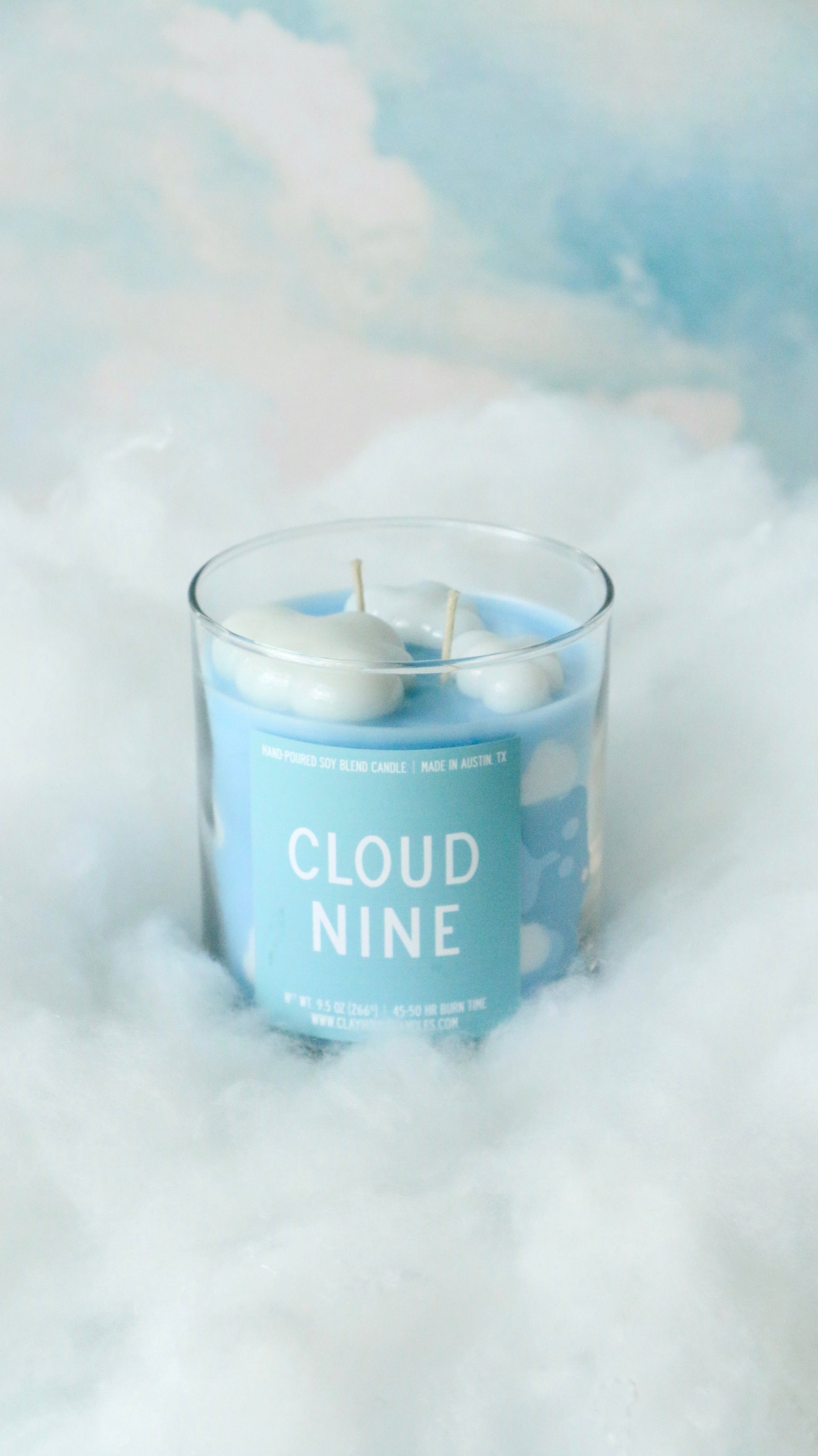 Candle labeled 'Cloud Nine' with a cloud-themed label on a soft, cloud-like background.