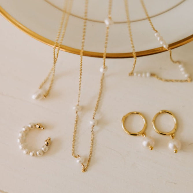 Gold and pearl jewelry set on a neutral background