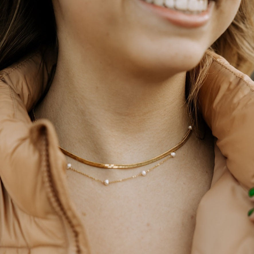Close-up of a person wearing a gold necklace with small pearls.
