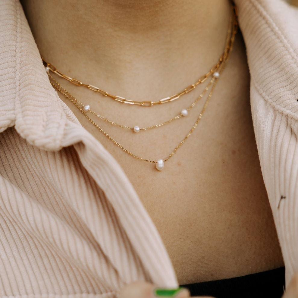 Close-up of a person wearing a gold chain necklace with pearl-like beads.