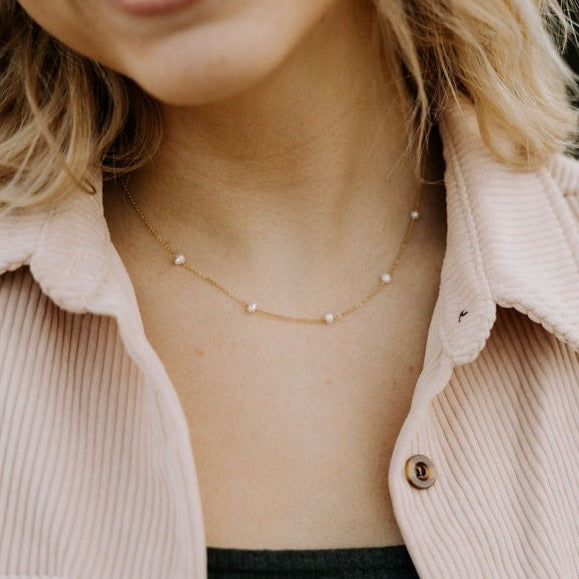 Close-up of a person wearing a delicate gold necklace with small pearls.