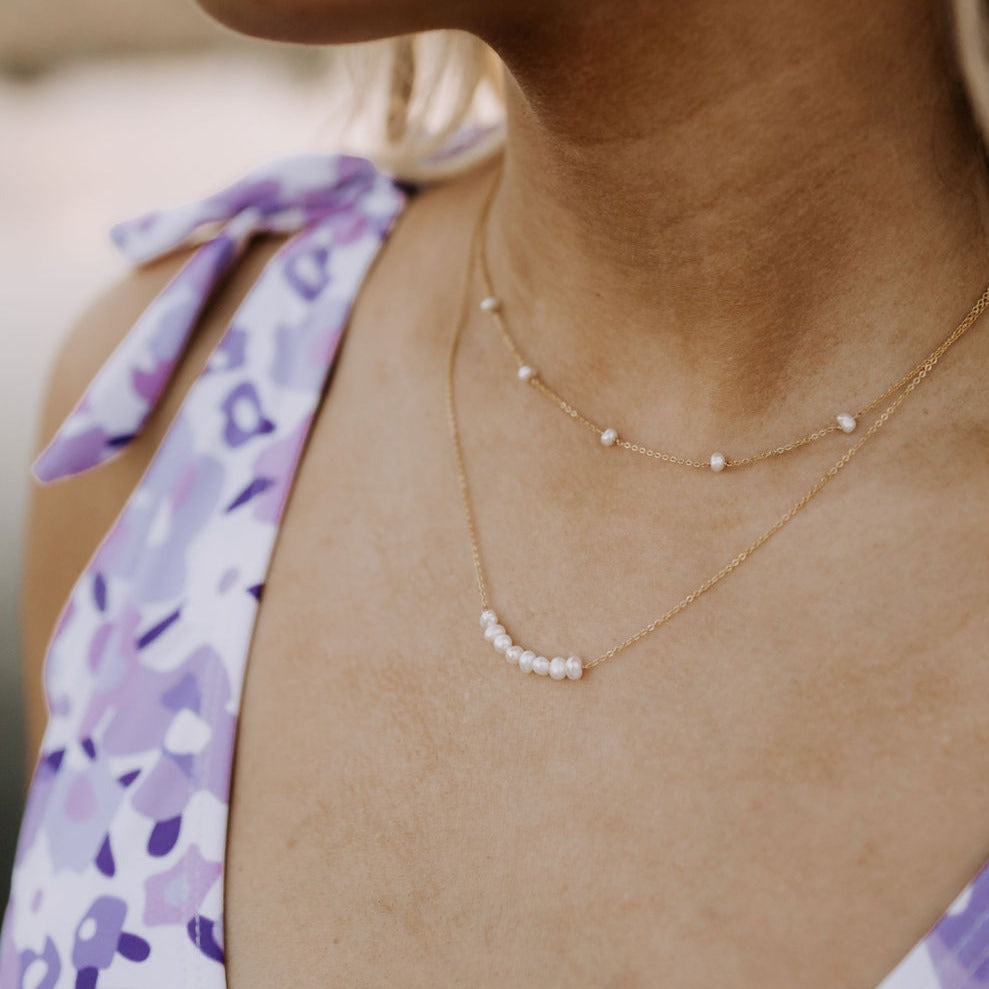 Close-up of a person wearing a delicate gold necklace with small pearls.