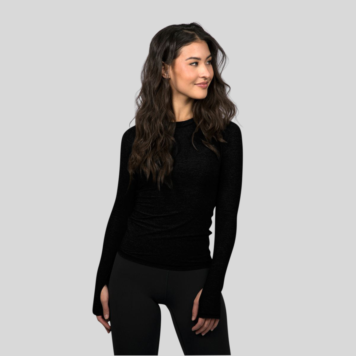 Woman wearing a black long-sleeve top and black leggings against a light gray background