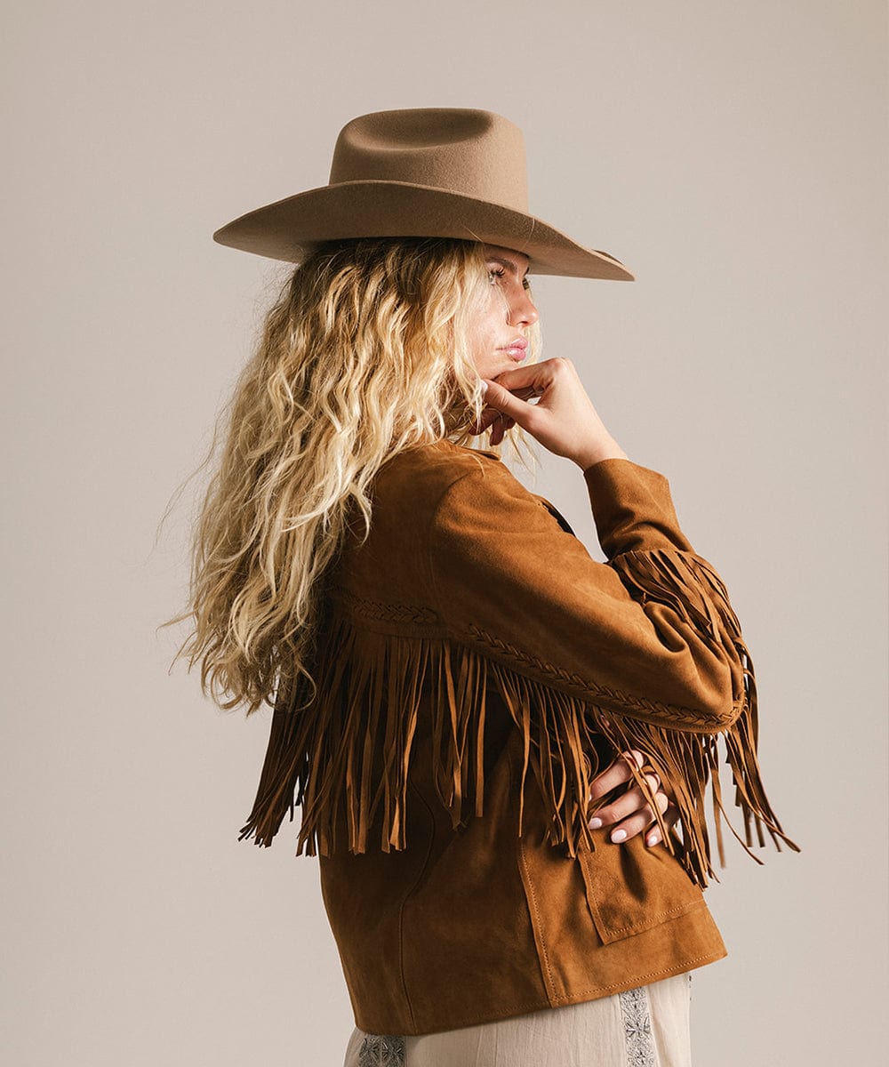 Woman wearing a brown fringed jacket and hat against a plain background