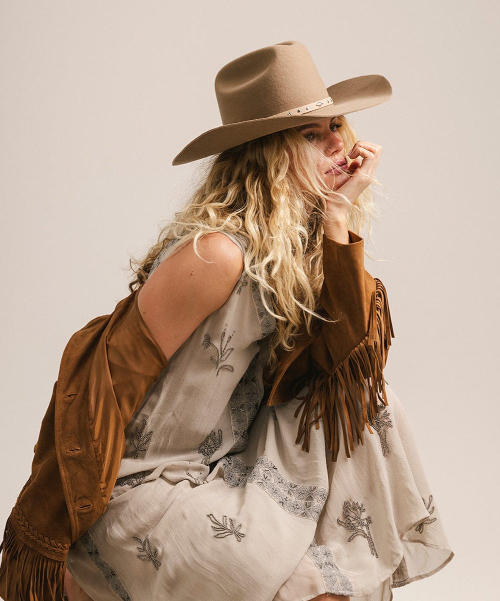 Woman wearing a cowboy hat and brown jacket with a white background