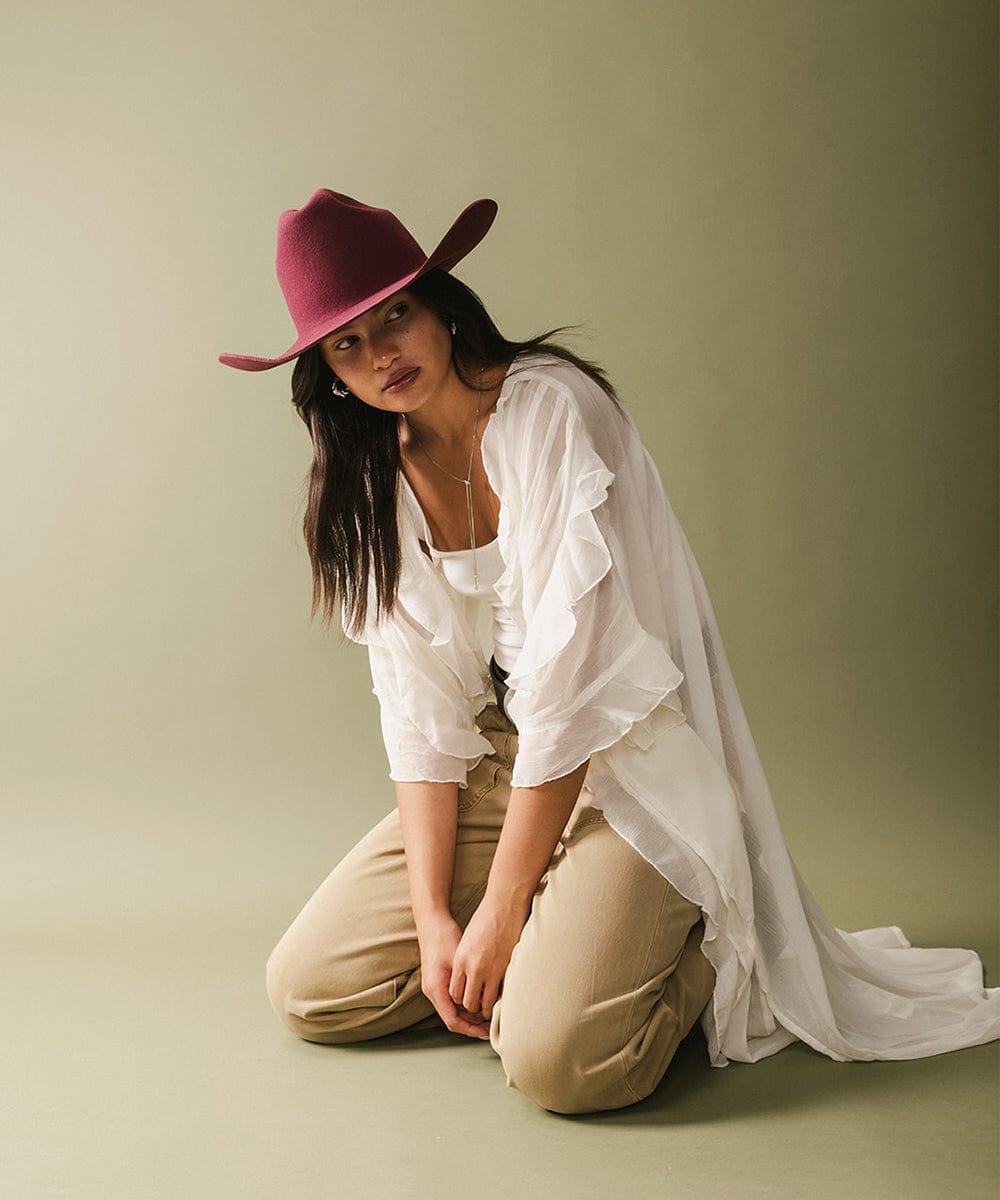 Woman wearing a white blouse and beige pants with a red hat on a plain background