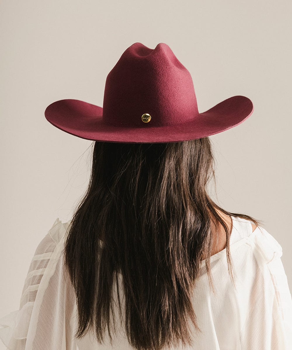 Person wearing a burgundy cowboy hat with a beige background