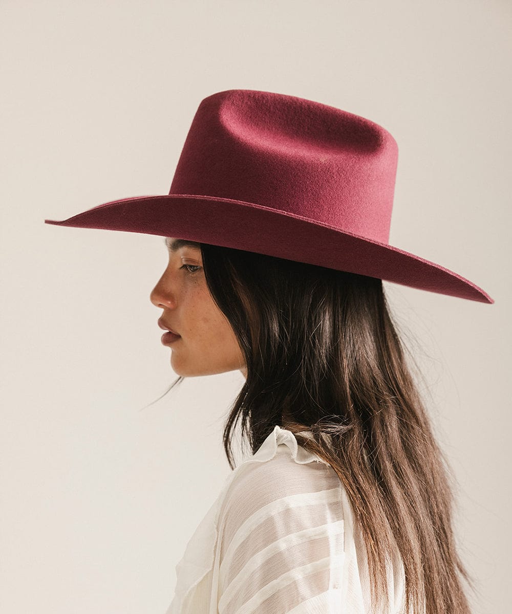 Woman wearing a burgundy wide-brimmed hat against a neutral background