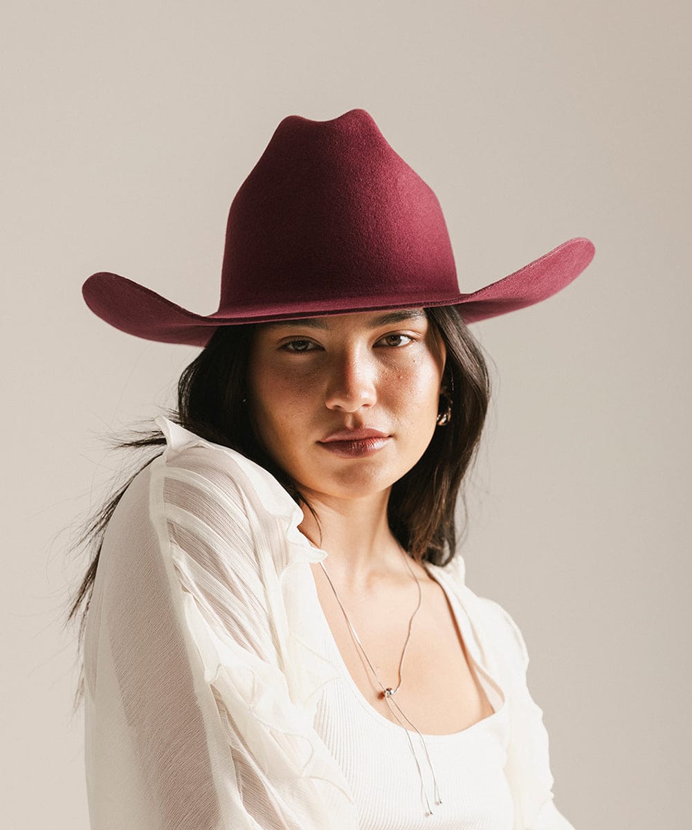 Woman wearing a maroon cowboy hat against a plain background