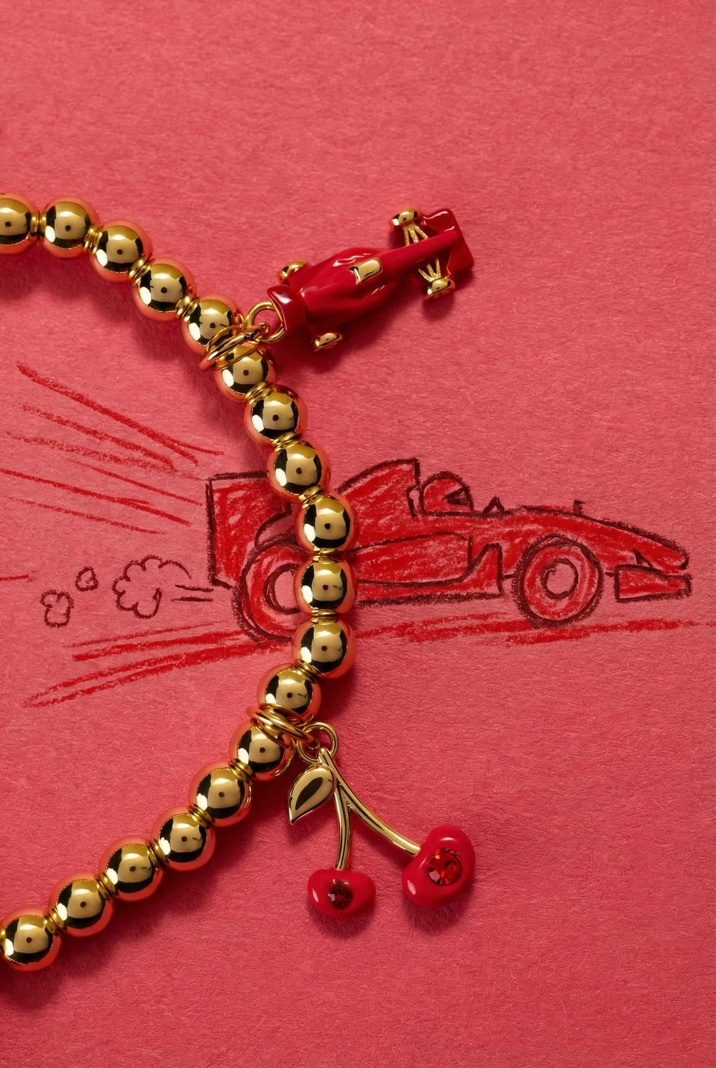 Gold beaded bracelet with cherry charms on a red background with race car illustrations