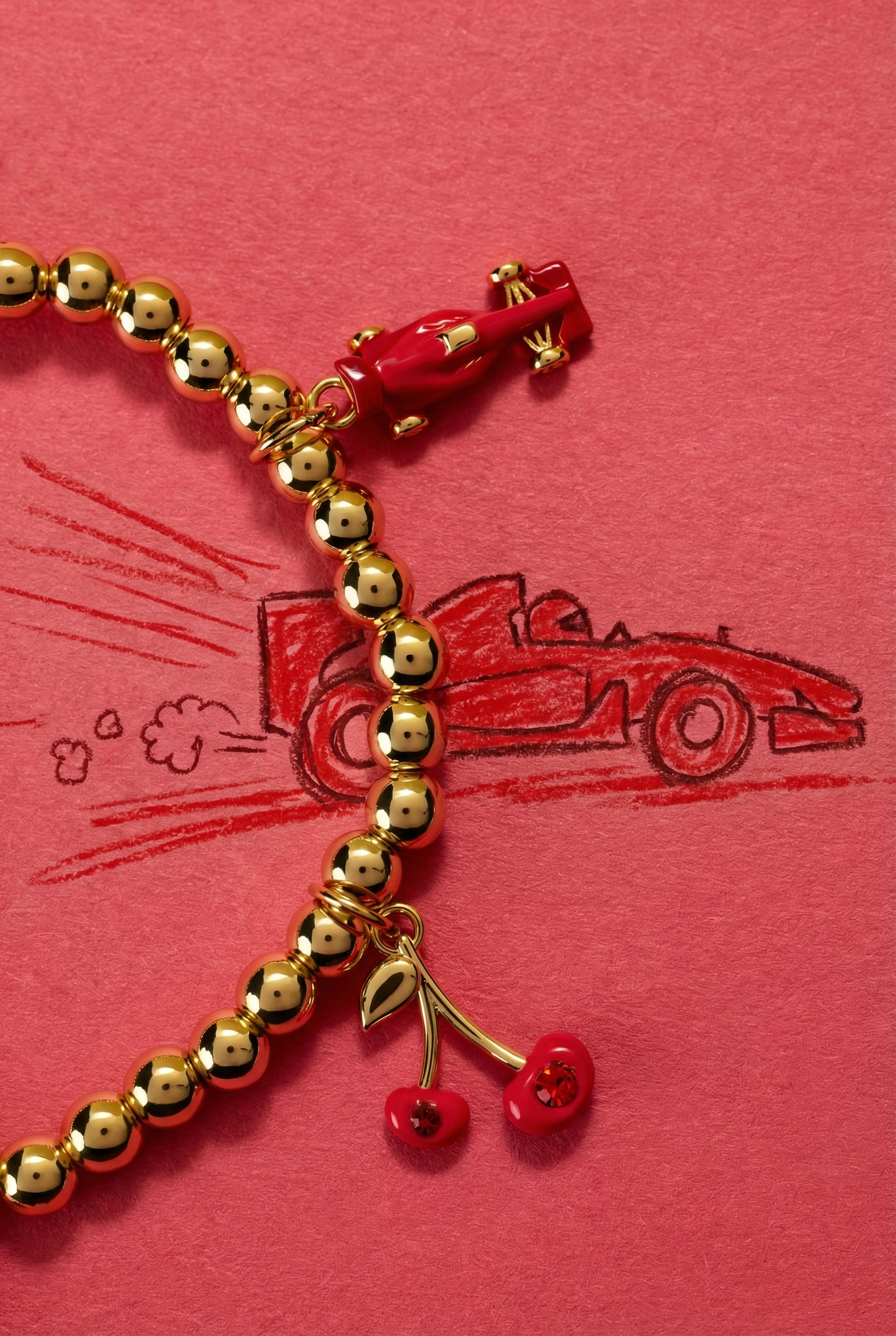 Gold beaded bracelet with cherry charms on a red background with race car illustrations
