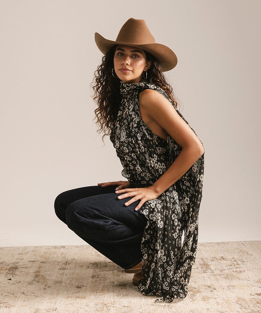 Woman wearing a floral dress and brown cowboy hat against a plain background